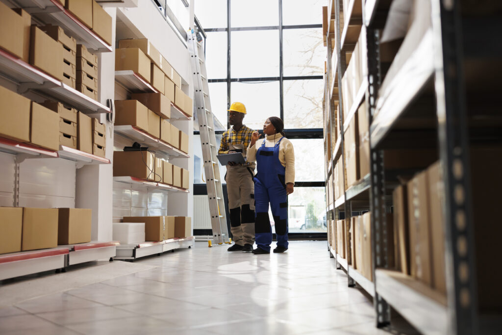 African american warehouse distribution manager doing inventory with assistant