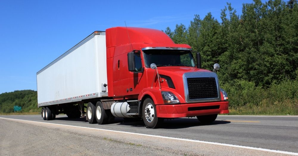 Red semi-truck with white trailer driving on a highway.
