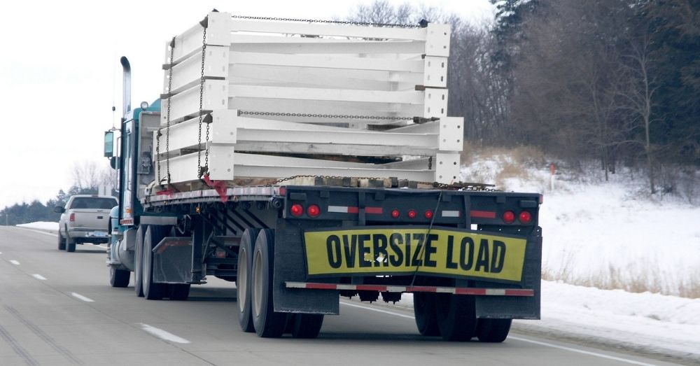 Flatbed truck with "OVERSIZE LOAD" banner hauling steel.