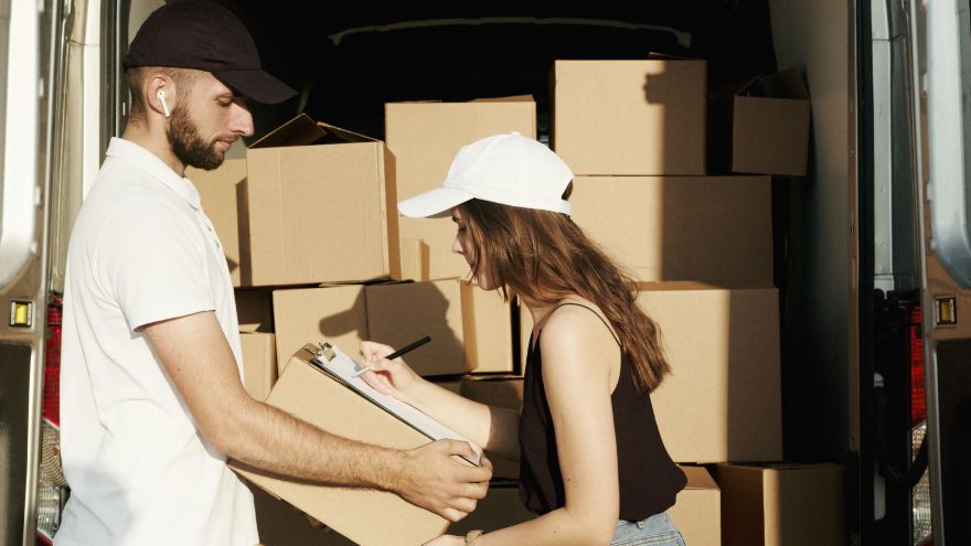 Two people loading cardboard boxes into a delivery van while the woman signs a clipboard — storage solution.