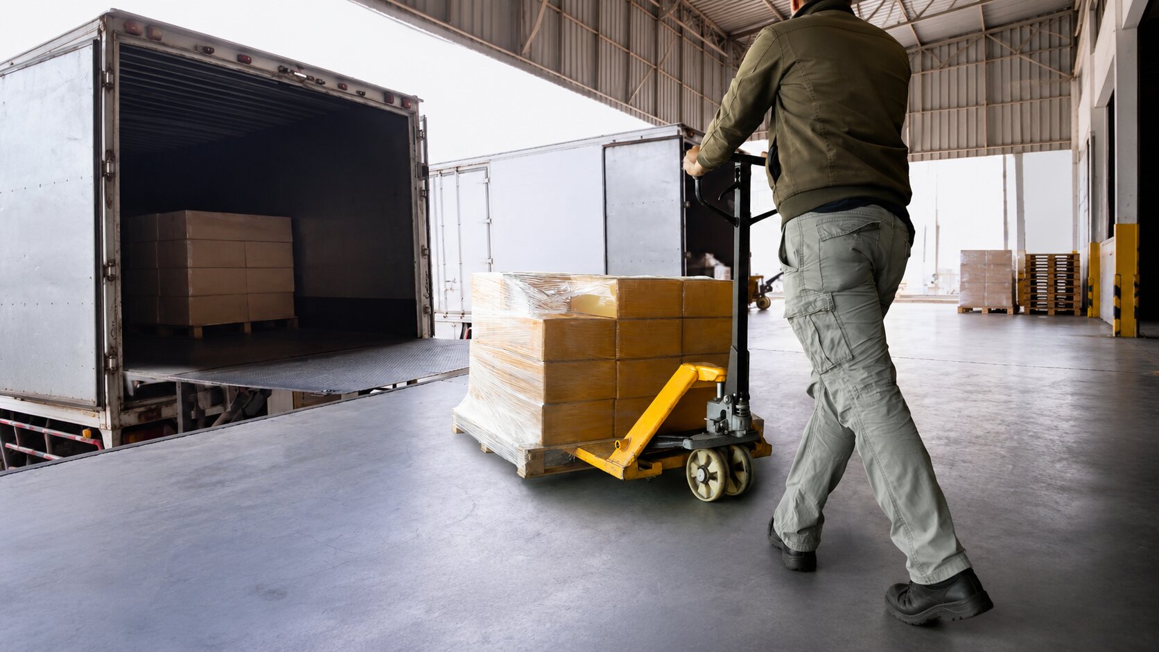 Worker moving palletized boxes from a truck at a warehouse loading do.