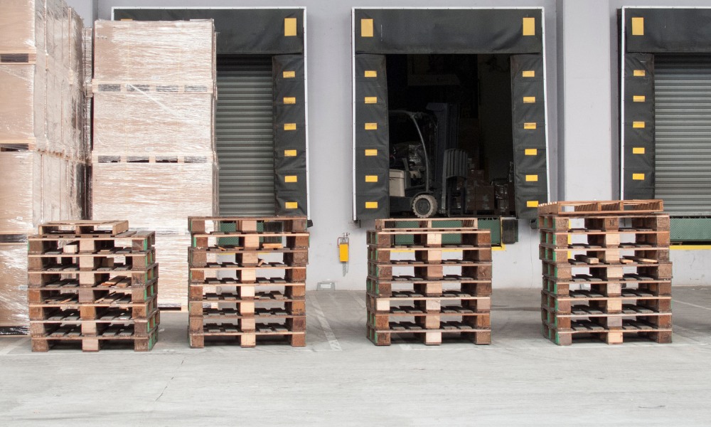 Four stacks of empty wooden pallets lined up outdoors in front of warehouse