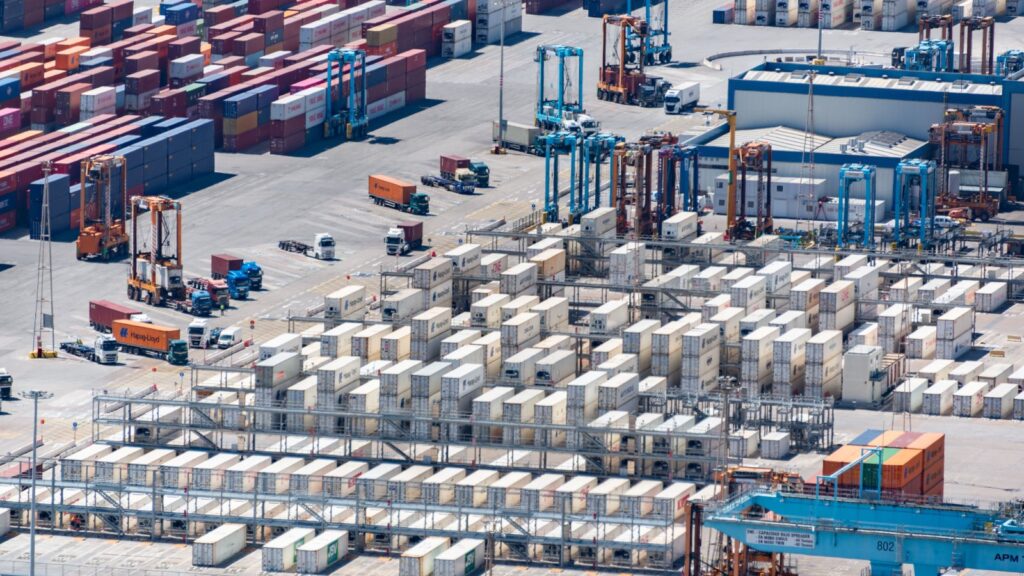 Aerial view of a busy cargo port with stacked containers and logistics machinery, representing key logistics infrastructure.
