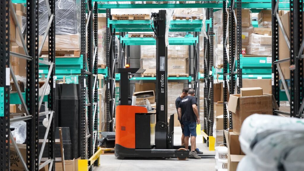 Modern warehouse operations with employees and forklift navigating aisles for logistics and inventory management